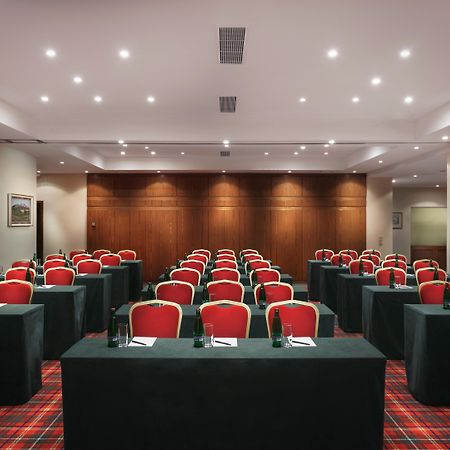 Art Nouveau Palace Hotel Praga Esterno foto The photo displays a conference room set up for a meeting or event. The room features multiple rows of rectangular tables covered with dark green tablecloths. Each table is arranged with red chairs placed around them. The walls have a warm wood finis