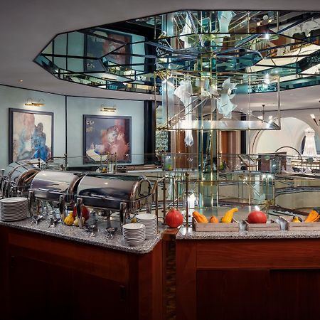 Art Nouveau Palace Hotel Praga Esterno foto The photo shows a luxurious restaurant interior featuring a central buffet area. The buffet is set on a polished wooden counter with a granite surface, displaying several chafing dishes. Above the buffet, there is an eye-catching mirrored structure t