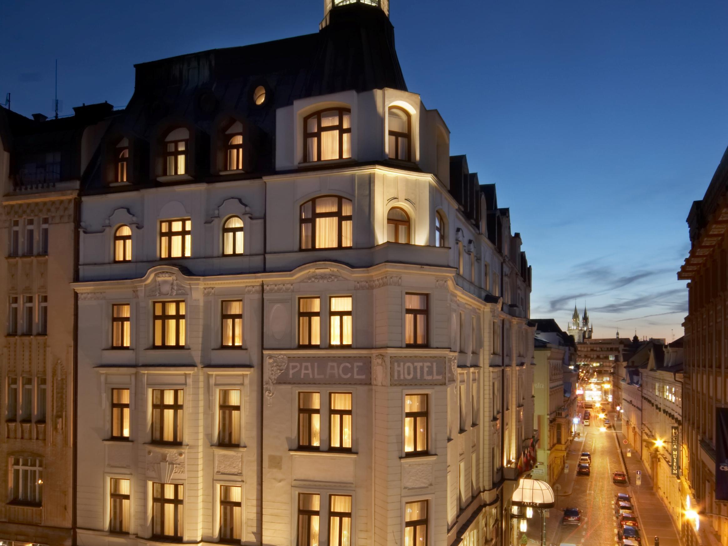 Art Nouveau Palace Hotel Praga Esterno foto The image shows a hotel building, likely named "Palace Hotel," illuminated against the evening sky. The architecture appears elegant, with a mixture of traditional and modern design elements. Street lights illuminate the surrounding area, and you can