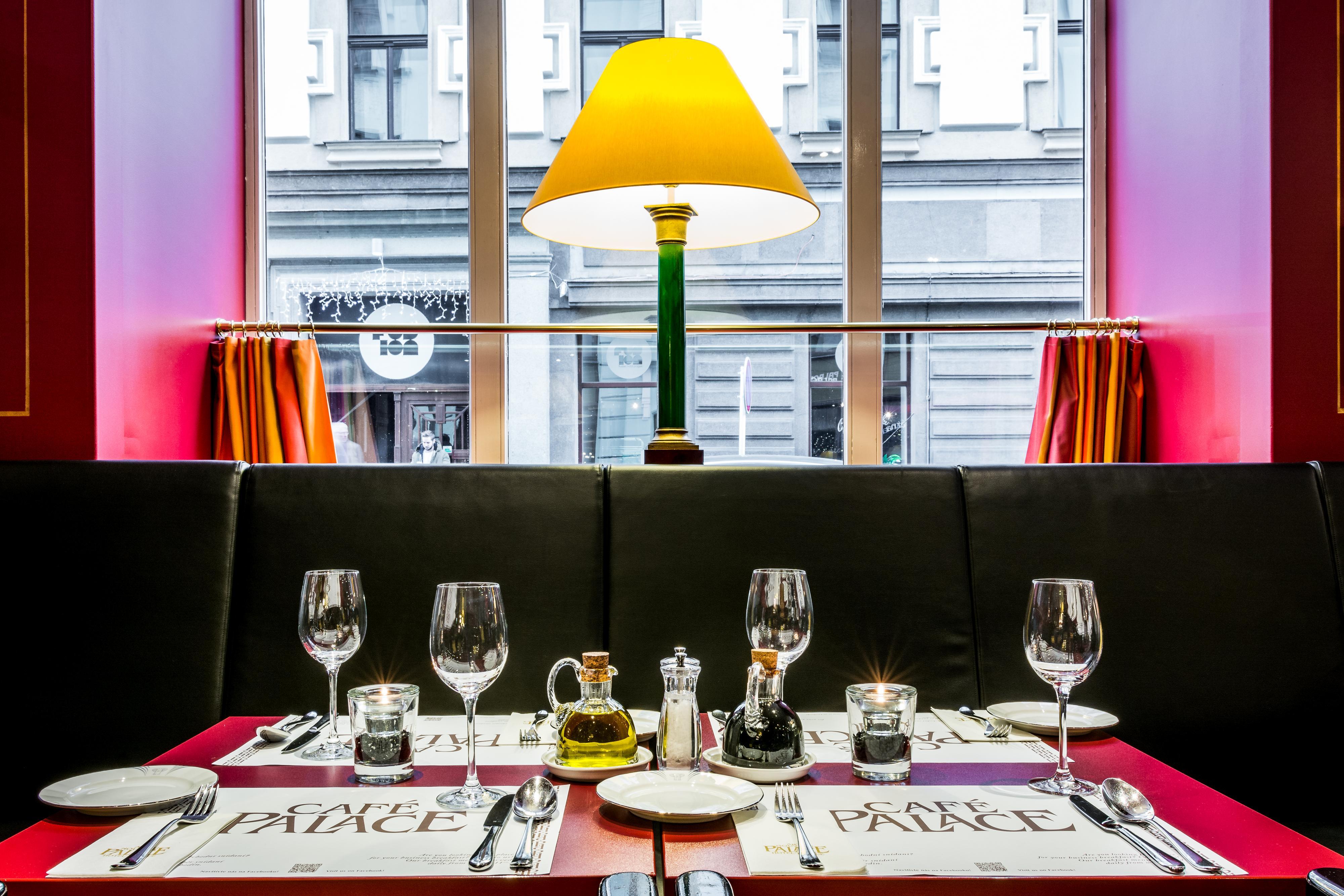 Art Nouveau Palace Hotel Praga Esterno foto The photo shows a dining table set up in a restaurant. The table is covered with a red tablecloth and has several glassware pieces, including wine glasses and water glasses. There are also condiments like salt and pepper shakers, as well as a small o