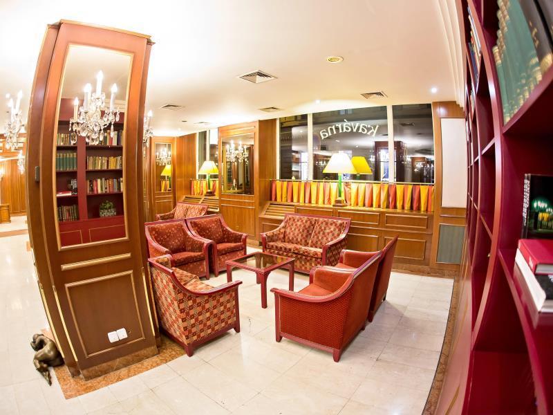 Art Nouveau Palace Hotel Praga Esterno foto The photo depicts an elegant seating area, likely within a hotel or a lounge. It features several plush, red upholstered chairs arranged around a small table. In the background, there are tall bookshelves filled with books, and decorative elements li
