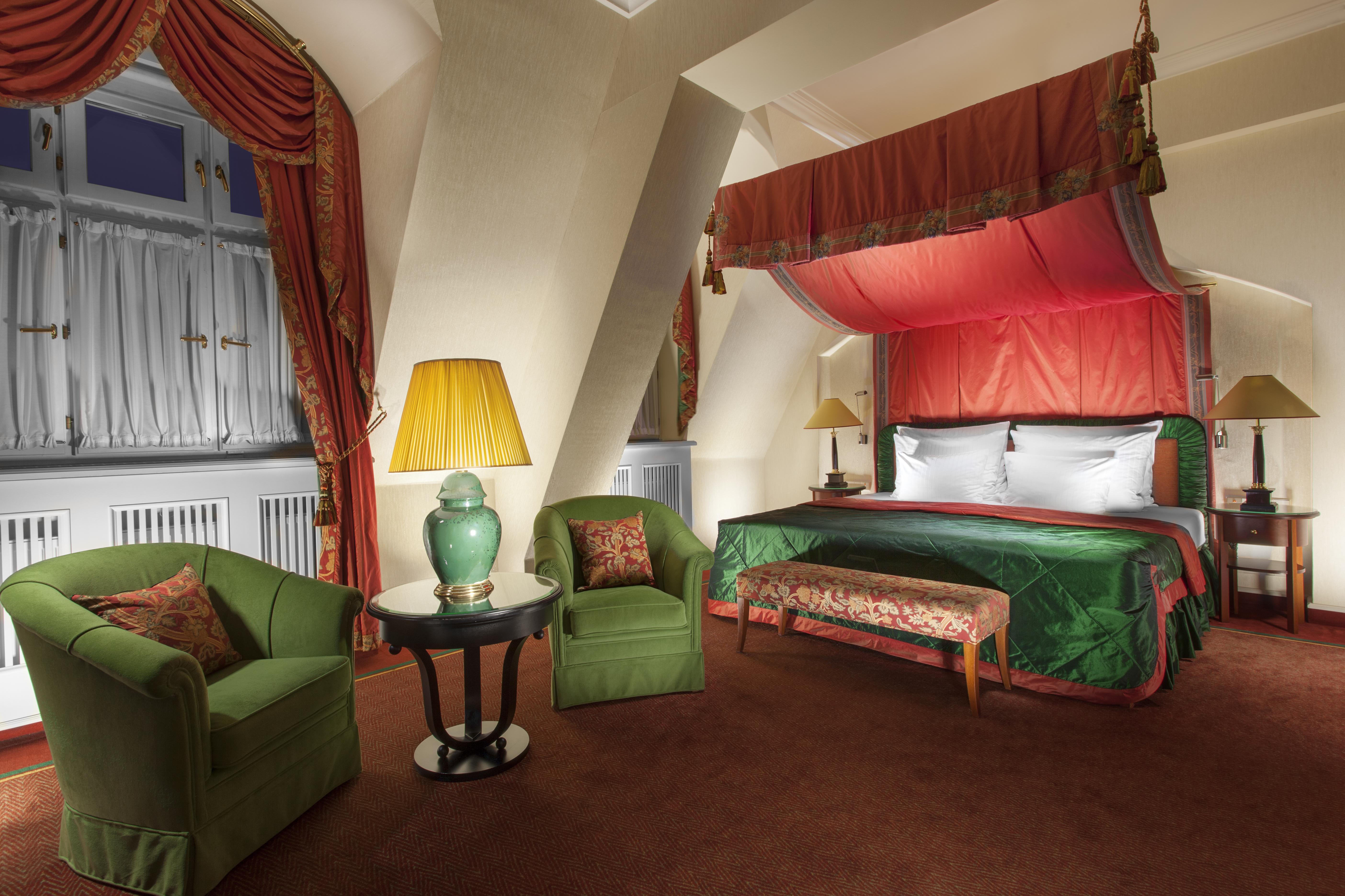 Art Nouveau Palace Hotel Praga Esterno foto The photo shows a luxurious hotel room featuring a large bed with a colorful canopy. The bed is adorned with elegant linens and pillows. On either side of the bed, there are stylish lamps providing warm light. 

In the foreground, there are two green