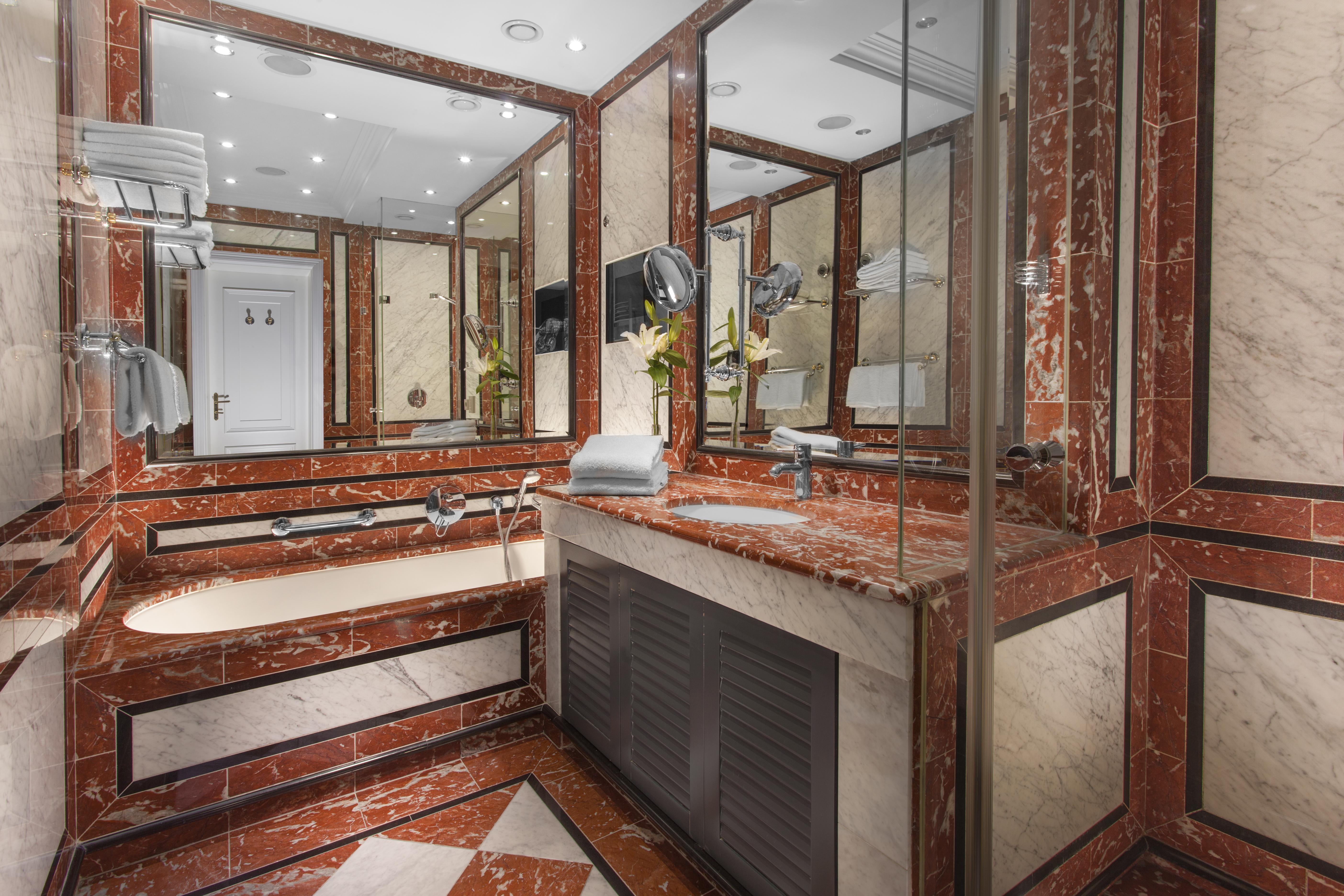 Art Nouveau Palace Hotel Praga Esterno foto The photo shows a luxurious bathroom featuring a combination of marble finishes in warm tones, including red and cream. There is a bathtub integrated into the design, along with a sink area that has a large countertop. The walls are adorned with mirr