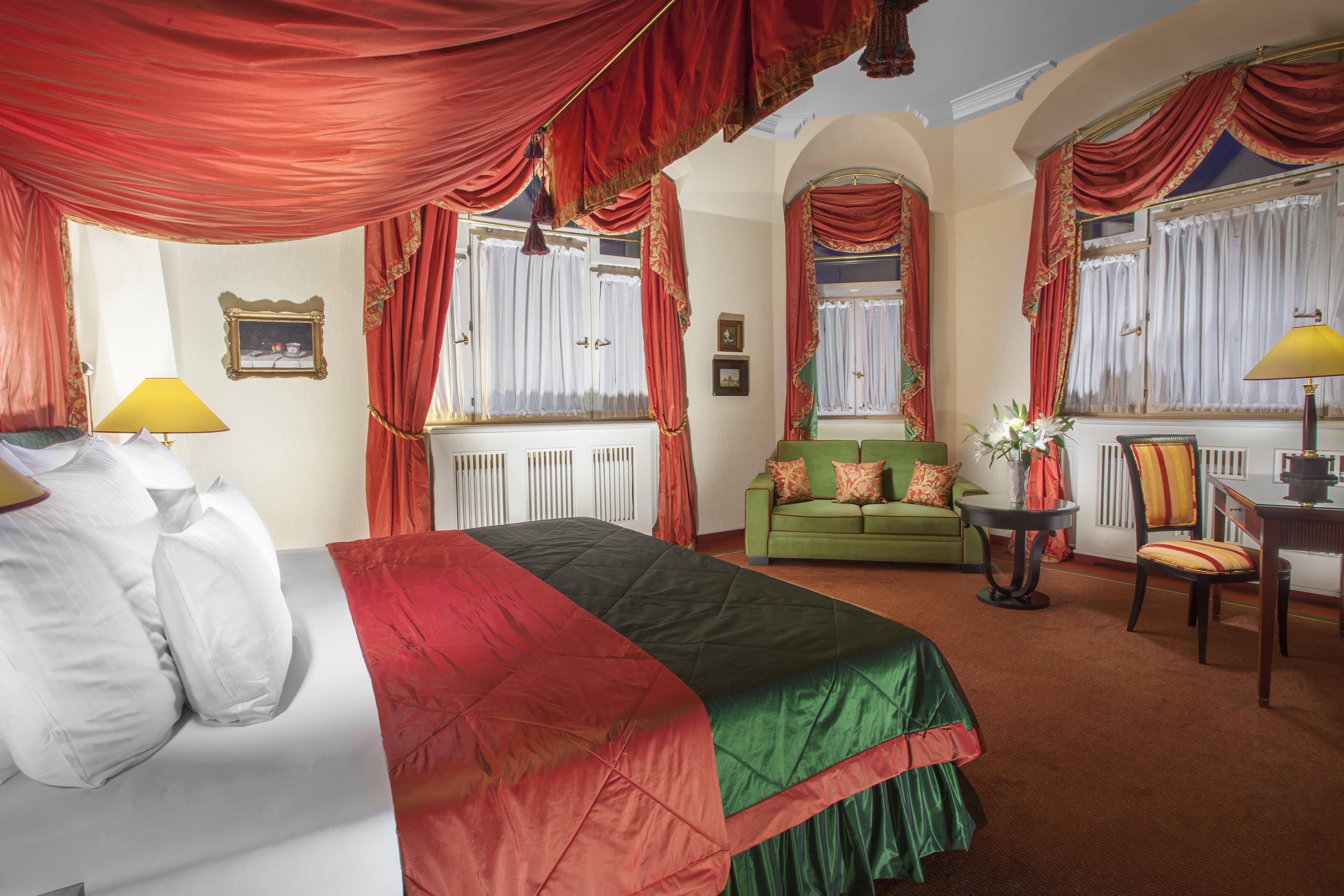 Art Nouveau Palace Hotel Praga Esterno foto The photo shows an elegant hotel room featuring rich colors and luxurious decor. There is a large bed with decorative bedding, primarily in red and green hues. Above the bed, ornate drapery adds a touch of sophistication. 

To the side, a comfortable