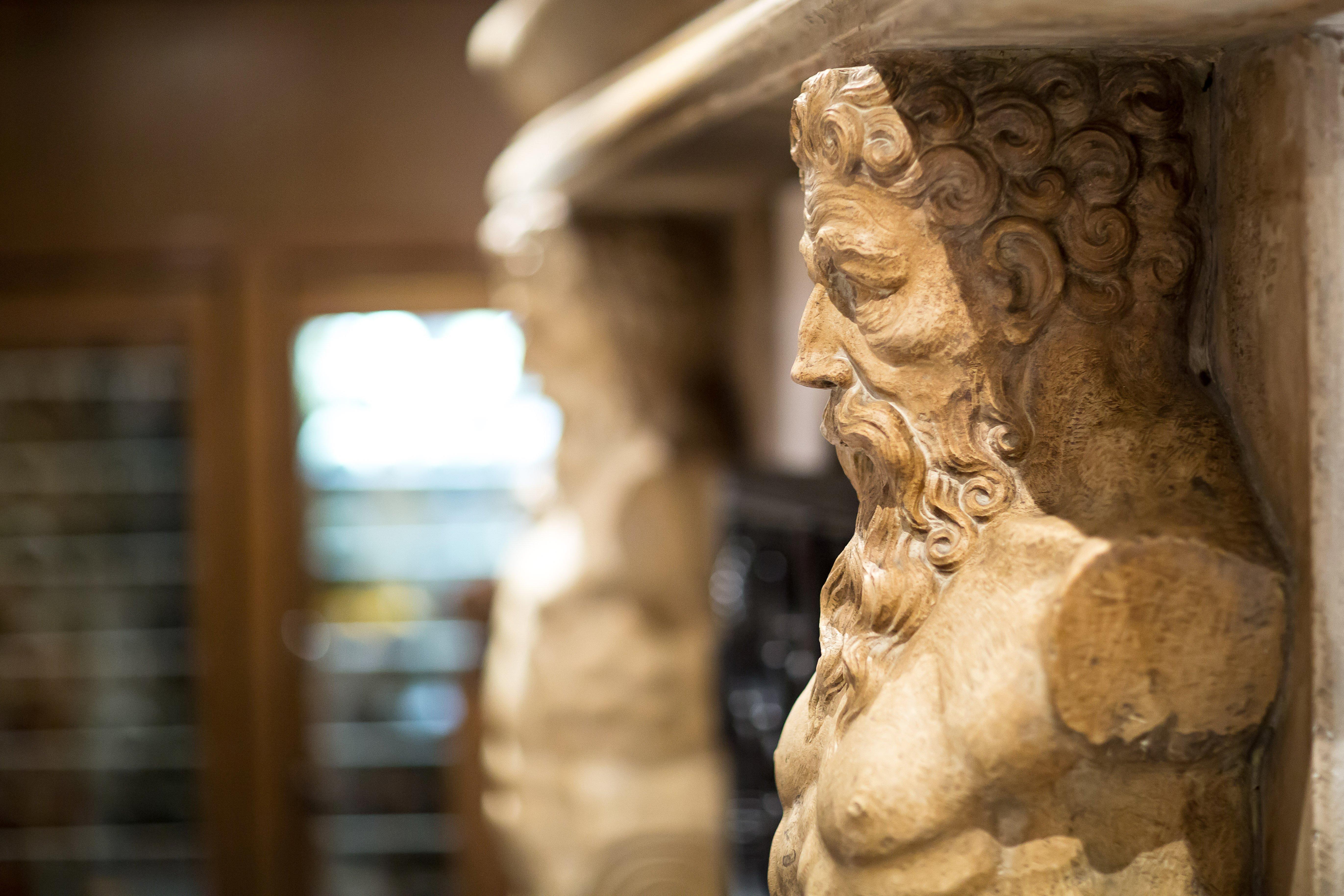 Art Nouveau Palace Hotel Praga Esterno foto The photo shows a close-up of a carved stone column or support with a depiction of a bearded figure. The figure appears to have a muscular build and is likely stylized in a classical or ancient artistic manner. The background is slightly blurred, sug