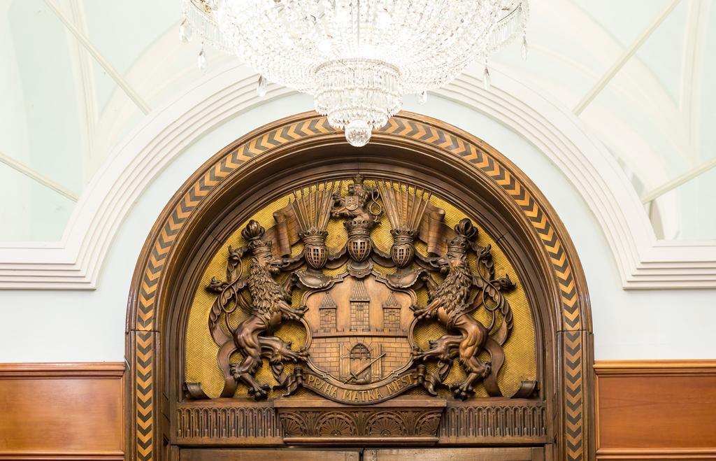 Art Nouveau Palace Hotel Praga Esterno foto The photo shows an ornate wooden archway, featuring a detailed carving at the top. This carving includes two heraldic figures, likely representing lions, flanking a central shield or emblem. Above this shield, there are decorative elements, including