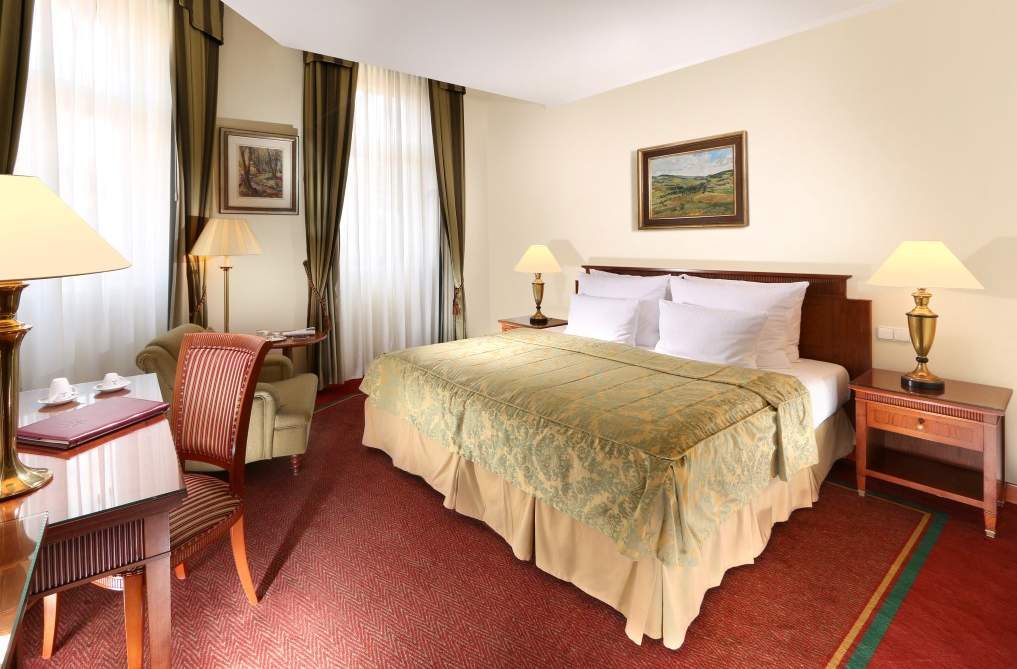 Art Nouveau Palace Hotel Praga Esterno foto The photo shows the interior of a hotel room. It features a neatly made bed with a light green bedspread and white pillows. To the side, there's a bedside table with a lamp. A painting hangs on the wall above the bed, depicting a landscape. The room 